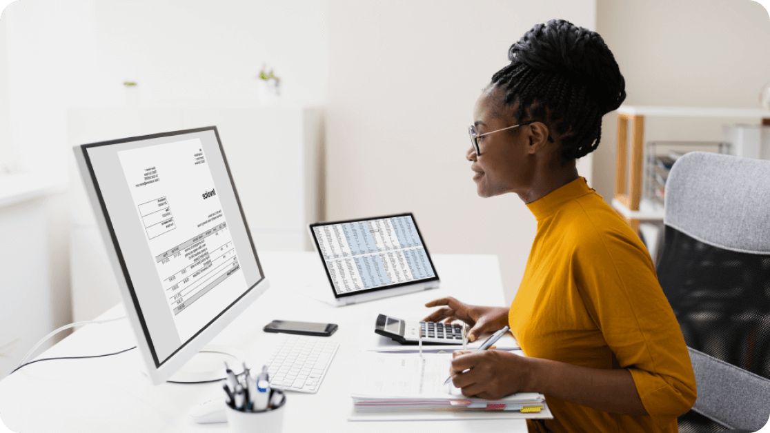Person using a calculator and working on multiple devices at their desk.
