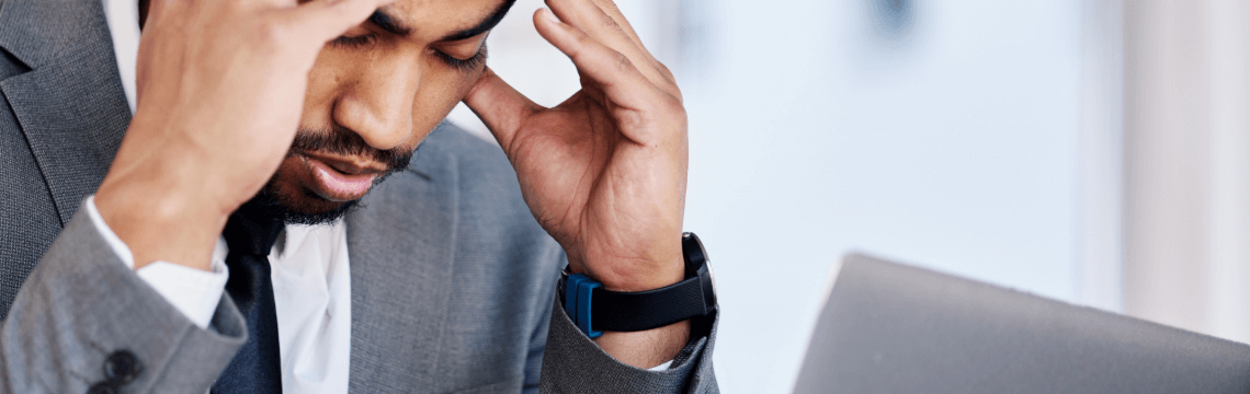 Frustrated tax researcher with hands on temples, looking down at laptop