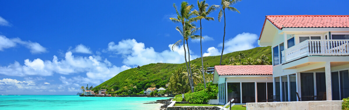 Oceanfront home on Oahu, Hawaii overlooking turquoise waters, with swaying palm trees and blue skies. 