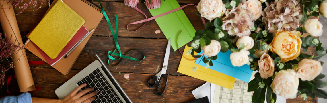 Person typing on laptop with a desk full of flowers and craft materials