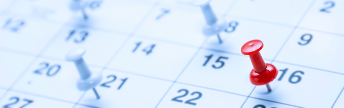 Red and white thumb tacks marking dates on a calendar.