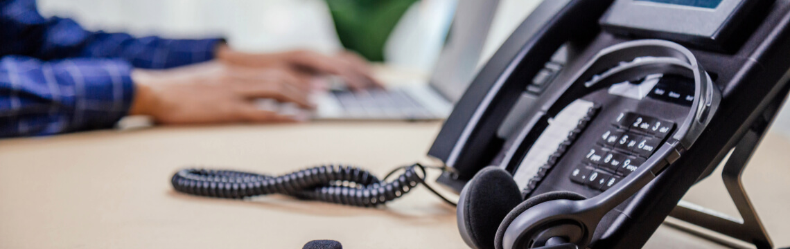 Phone and headset on a desk with a person in the background.