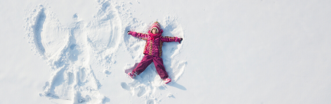 Child dressed in red making snow angels.