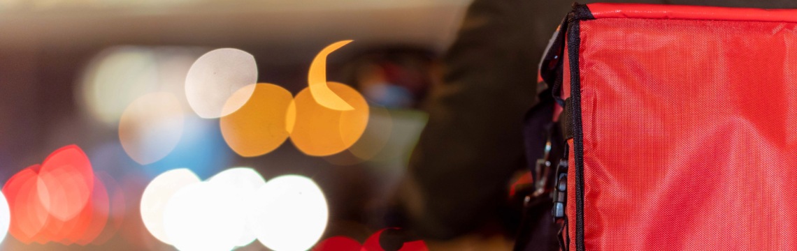 Person on a motorcycle delivering food in a city at night.