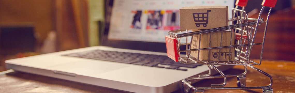Miniature shopping cart with box inside of it in front of an open laptop